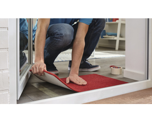 Muž pokládá červený koberec v domě.