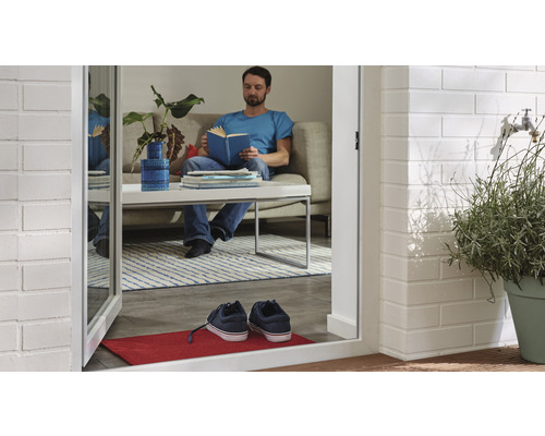 "Pohled skrze otevřené dveře na muže sedícího na pohovce a čtoucího knihu