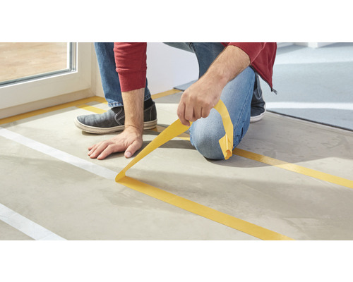 Řemeslník lepí maskovací pásku na podklad.