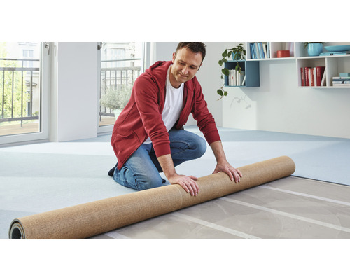 Muž pokládá koberec na podklad v interiéru.