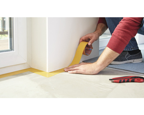 Osoba připevňuje rohem krycí pásky roh v místnosti.