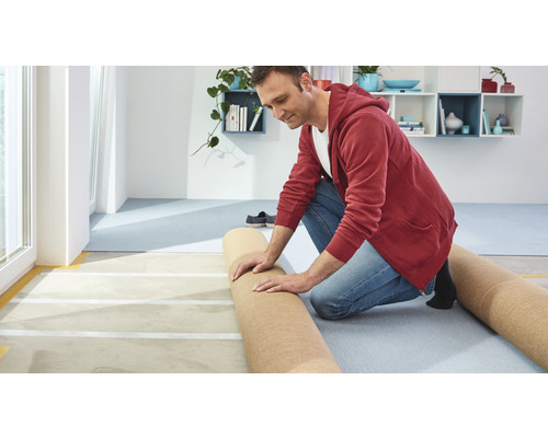 Muž pokládá koberec ve světlé místnosti.