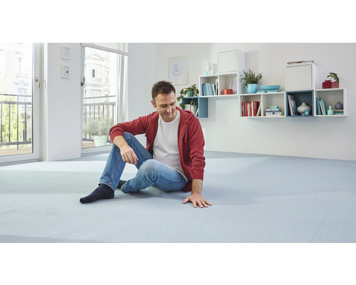 Muž sedí na světlém koberci ve světlé místnosti s policemi na stěně