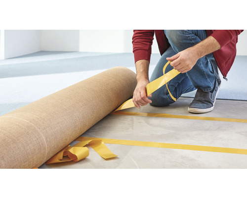 Muž pokládá koberec pomocí oboustranné lepicí pásky.
