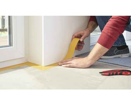 Osoba nanáší malířskou pásku na zeď, aby chránila povrchy před barvou.