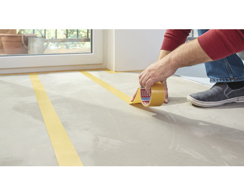 Osoba lepí maskovací pásku na podlahu.