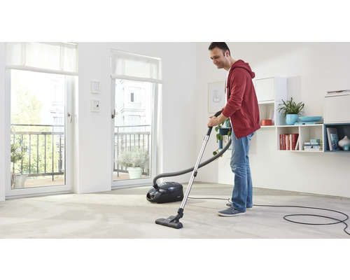 Muž vysává podlahu v jasném pokoji pomocí vysavače.