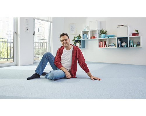 Muž sedí na světlém koberci ve světlé místnosti s policemi