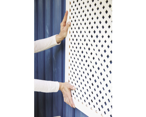 Osoba montuje bílou mřížku krytu radiátoru s kosočtvercovým vzorem