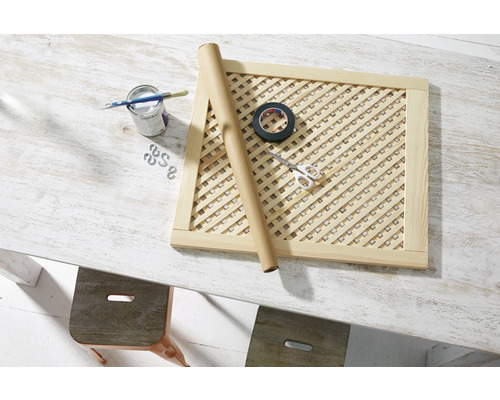 Dřevěný mřížkový rám s malířskými potřebami, lepicí páskou a nůžkami na stole.