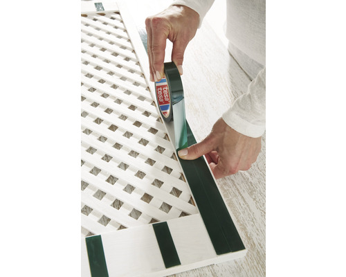 Osoba aplikuje lepicí pásku Tesa na bílou mřížku.