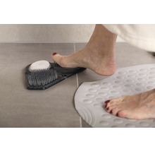 Noha na vaničce na nohy s kartáči a pemzou vedle koupelnové rohože