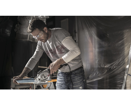 Muž s ochrannými brýlemi řeže prkno pomocí okružní pily Worx