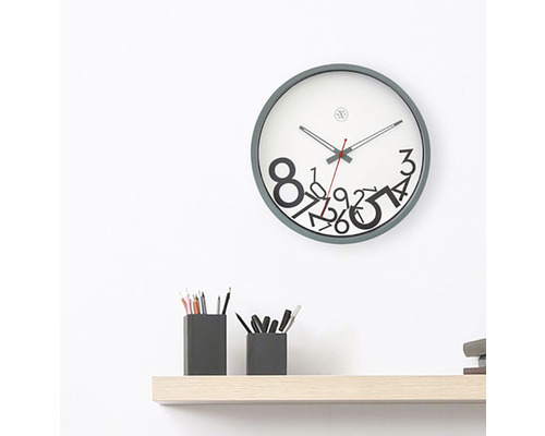 Nástěnné hodiny s číselným vzorem nad policí s držáky na pera