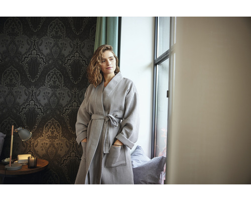 Žena v šedém vaflovém županu v místnosti s tapetou se vzorem