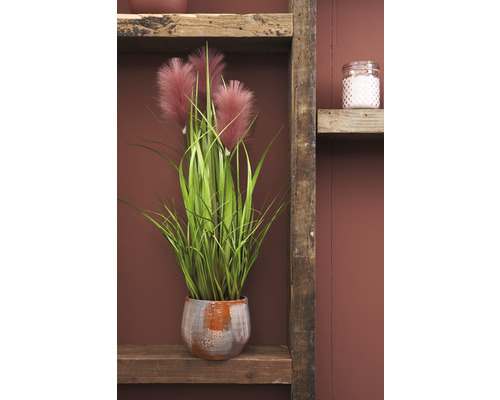 Dekorativní umělá rostlina s peříčky v květináči na dřevěné polici