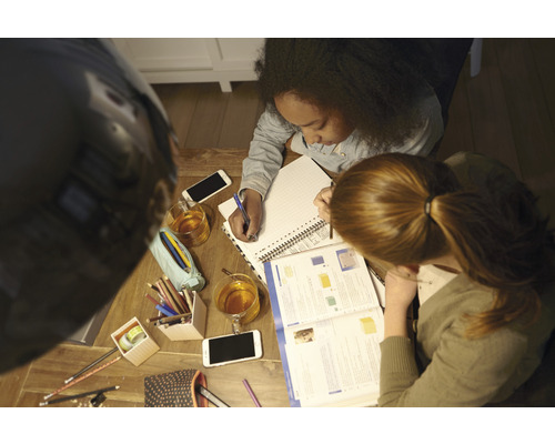 Dvě osoby se společně učí u dřevěného stolu s poznámkovými bloky, tužkami, mobilními telefony a nápoji.