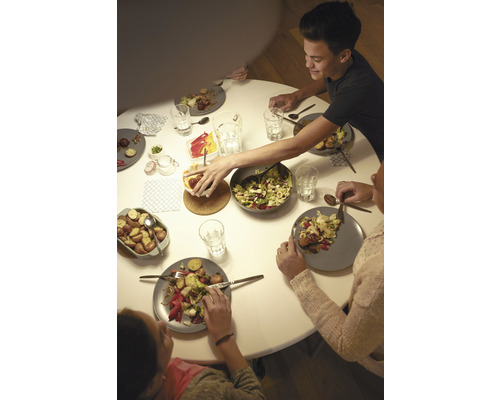 Rodina sedí u kulatého stolu a jí saláty a brambory.