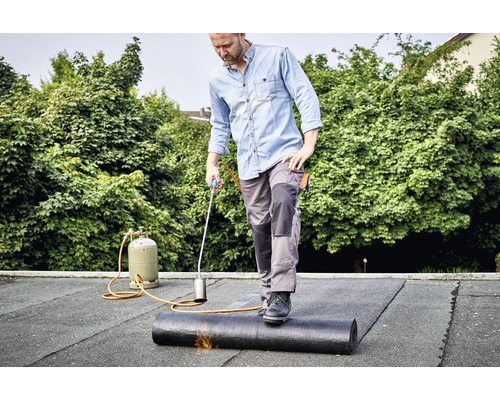 Muž pokládá střešní pásku na střechu pomocí hořáku.
