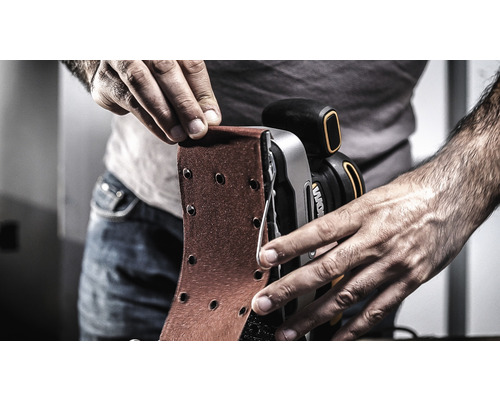 Osoba mění brusný papír na pásové brusce.