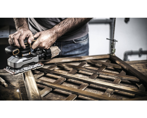 Osoba brousí dřevěnou mřížku pomocí vibrační brusky.