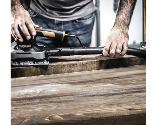 Muž brousí dřevěnou desku pomocí multifunkční brusky s odsáváním prachu od firmy Worx