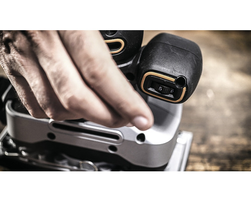 Detailní záběr muže ovládajícího vibrační brusku.