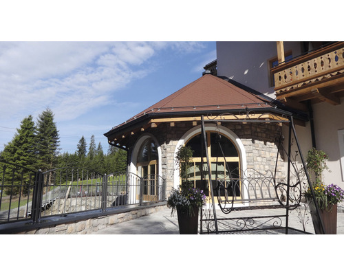 Vnější pohled na dům s kamennou zdí, hnědou střechou a zábradlím z tepaného železa