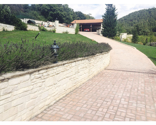 Příjezdová cesta k domu s kamennou zdí a dlažebními kostkami.