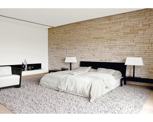 Ložnice s postelí, křeslem, kobercem a kamennou zdí