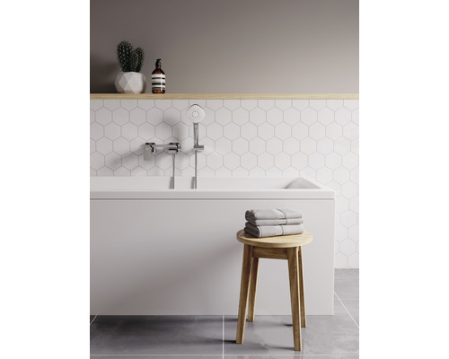 Světlá koupelna s vanou, ruční sprchou, ručníky a dřevěnou stoličkou.