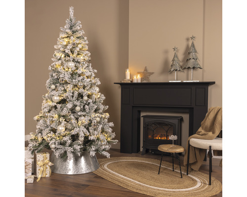 Slavnostně vyzdobený pokoj se zasněženým vánočním stromkem, krbem a dekoracemi.