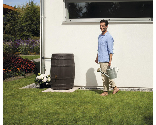 Sud na dešťovou vodu ve vzhledu sudu vedle muže s konví na zalévání na zahradě.