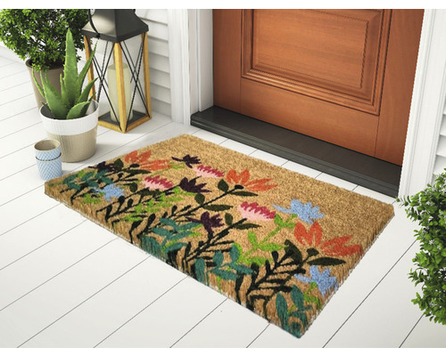 Kokosová rohožka s květinovým vzorem před vchodovými dveřmi.