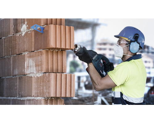 Stavební dělník řeže cihly mečovou pilou. Jsou používány osobní ochranné pomůcky.