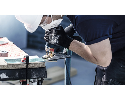 Řemeslník řeže dlaždici přímočarou pilou.