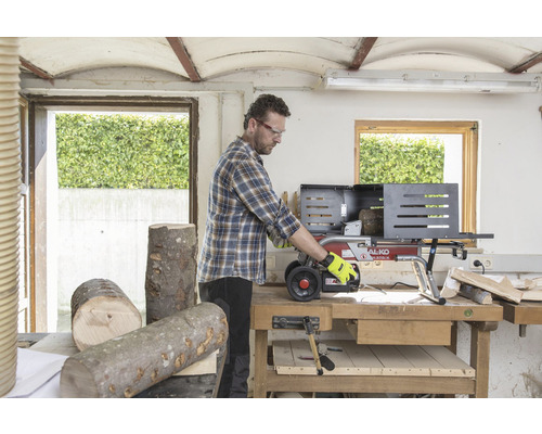 Muž pracuje s štípačkou dřeva v dílně. Polena leží na stole.