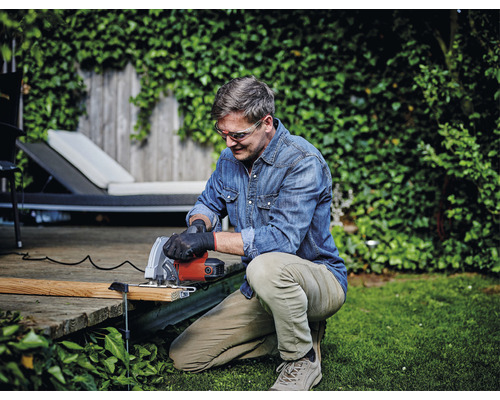 Muž pracuje na zahradě s ruční okružní pilou a má ochranné brýle.
