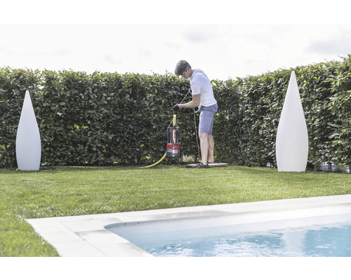 Muž obsluhuje kalové čerpadlo na zahradě poblíž bazénu, po stranách jsou dvě dekorativní svítidla.