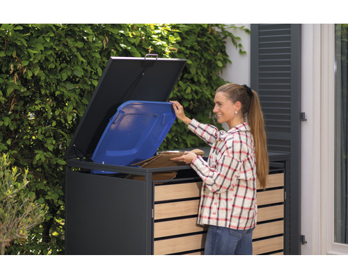 Žena plní šedý kontejner na popelnice modrou popelnicí a kartonem