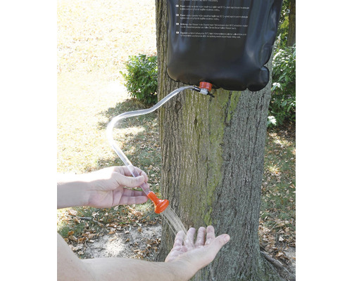 Přenosná sprcha s kapkami vody v ruce před stromem