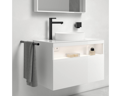 Moderní koupelna s bílou umyvadlovou skříňkou, umyvadlem na desku, černou baterií a držákem na ručníky.