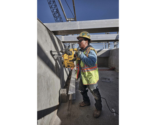 Stavební dělník vrtá vrtačkou otvor do betonové zdi na staveništi.