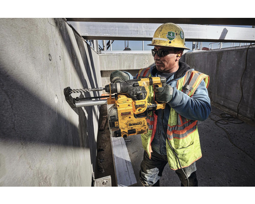 Stavební dělník vrtá vrtačkou DeWalt do betonové stěny na staveništi.