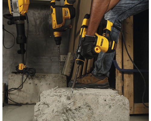 Řemeslník používá bourací kladivo DeWalt k opracování betonu. V pozadí jsou připravena další vrtací kladiva.