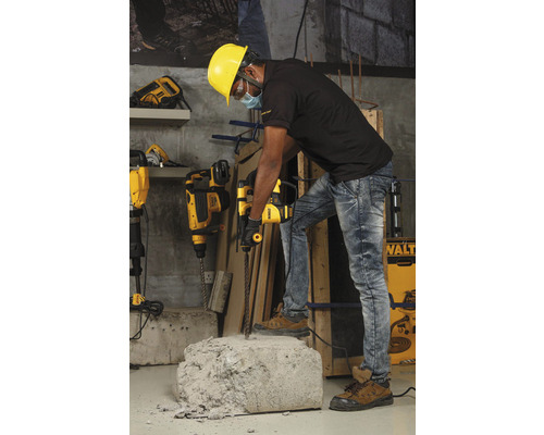 Dělník s ochrannou přilbou používá vrtací kladivo k opracování kusu betonu.