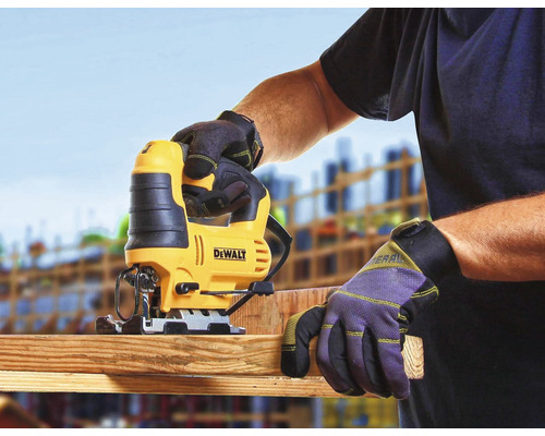 Přímočará pila řeže dřevěnou desku, obsluhuje ji osoba v pracovních rukavicích