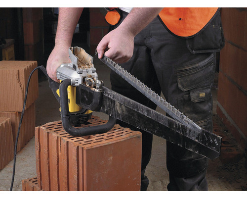 Muž montuje elektrickou řetězovou pilu na cihlu.