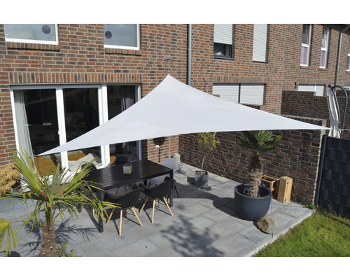 Terasa se sluneční plachtou, stolem a židlemi před cihlovým domem