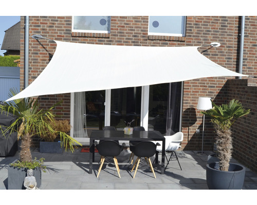 Bílá sluneční plachta nad terasou se stolem a židlemi
